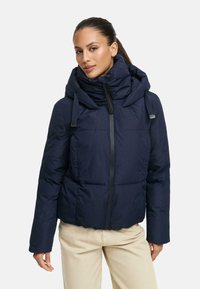 Navy puffer jacket with a high collar, front zipper, and large hood; features a quilted design and elastic drawstrings for adjustment.