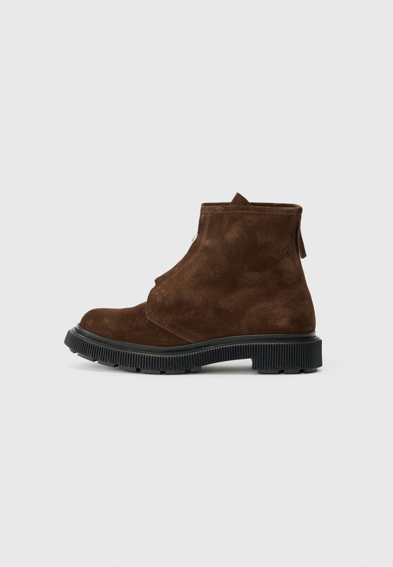 Bottines en daim marron avec une semelle en caoutchouc noir texturé, dotées d'une fermeture éclair et d'un design minimaliste. Surface supérieure lisse.