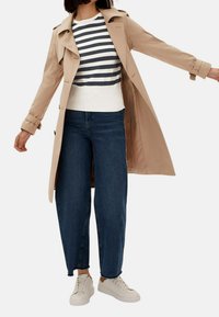 Trench coat beige con vita a cintura, maglione a righe chiare, jeans a gamba larga blu scuro e sneakers bianche. Tessuto liscio, design su misura.