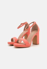 Coral high-heeled sandals with an open toe design, ankle strap, and block heel, made from smooth synthetic material.