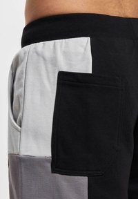 Black and gray color-blocked sweatpants with a textured fabric, featuring a large side pocket in a contrasting gray panel. Elastic waist.