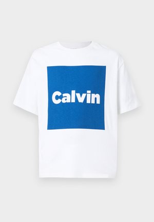 Witte T-shirt met korte mouwen, voorzien van een grote blauwe vierkant op de voorkant en de witte tekst "Calvin" gecentreerd in het vierkant.