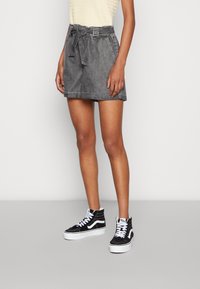 Shorts en denim gris avec une ceinture à nouer, des poches latérales et un ourlet replié. Associés à des baskets montantes noir et blanc.