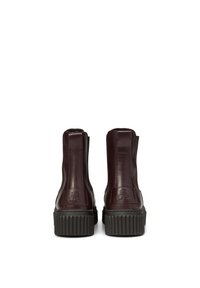 Bottines en cuir bordeaux avec une finition texturée. Comprend une semelle noire à relief prononcé et un détail de logo embossé sur le talon.