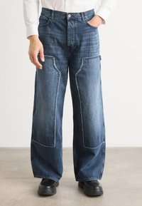 Denim cargo hlače s sproščenim krojem, svetlim in temno modrim pranjem ter značilnimi detajli patchwork. Dokončane s fridžanimi robovi in žepi.