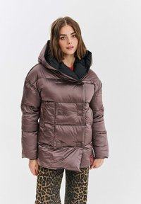 Brązowa pikowana kurtka puchowa z czarnym kapturem, z ukośnym zapięciem i strukturalnym wykończeniem. Połączona z spodniami w panterkę.