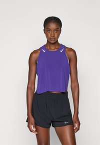 Fialová športová cropped tank top s bielymi akcentmi, doplnená čiernymi behacími šortkami so malým logom. Hladký materiál, voľný strih.