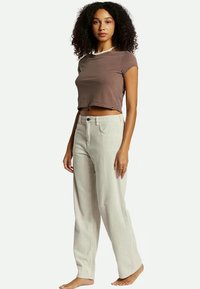 T-shirt corto marrone con maniche corte abbinato a pantaloni a palazzo a righe beige chiaro. Entrambi realizzati in un tessuto morbido e textured.