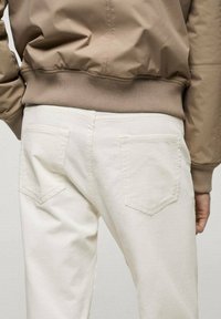 Pantaloni di velluto bianco con tasche posteriori, abbinati a un giubbotto bomber marrone chiaro con orlo e polsini a coste.