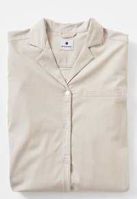 Camicia da pigiama a righe beige, design con bottoni, taschino sul petto, tessuto morbido e colletto con un'etichetta che indica la taglia M.