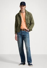 Πράσινο βαμβακερό μπουφάν, πορτοκαλί μπλούζα, φθαρμένο μπλε τζιν, μπλε αθλητικά παπούτσια και καπέλο. Διαθέτει τσέπες στο μπουφάν και ρολόι στον καρπό.