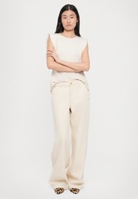 Beige sleeveless top with shoulder accents, paired with wide-leg beige pants and animal-print pointed shoes. Simple, clean design.