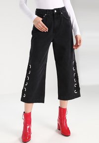Svarta denim culotte-byxor med sidogrommetdetaljer, hög midja och vida ben. Kombinerat med blanka röda ankle boots.
