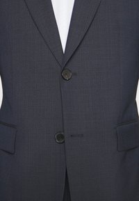 Granatowa marynarka w stylu garniturowym z teksturowanej tkaniny, z dwoma czarnymi guzikami i kieszeniami bocznymi. Zapewnia dopasowany krój z delikatnym wzorem i dobrze skrojoną sylwetką.