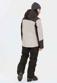 Veste de ski gris clair avec des accents gris foncé et une capuche, associée à un pantalon noir. Présente une texture lisse et un design décontracté.