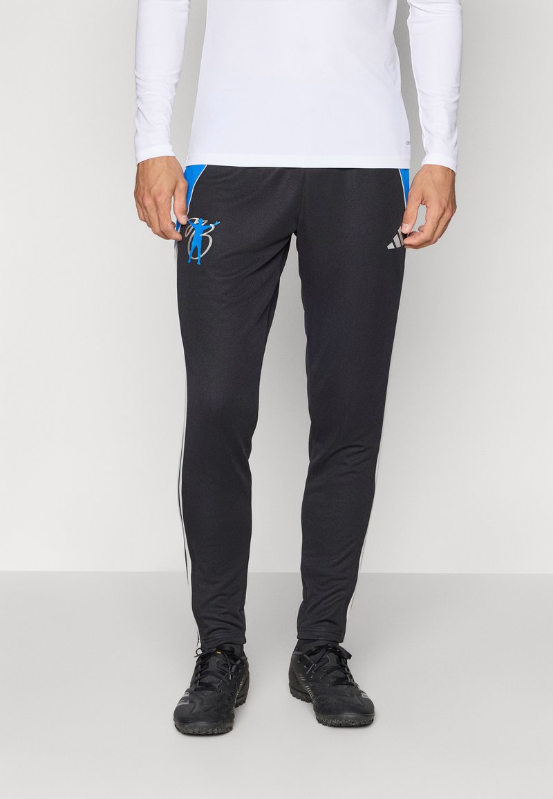 Pantaloni sport negri dintr-un material elastic, cu accente albastre, un emblemă și dungi laterale albe. Asortați cu pantofi sport negri.
