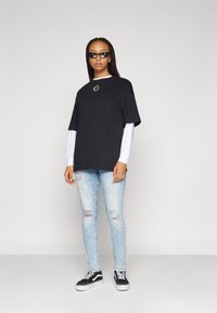 Crni oversized T-shirt s izvezenim motivom sunca, složen preko bijele majice dugih rukava. Uparen sa svijetloplavim isfinkanih trapericama i crnim tenisicama.