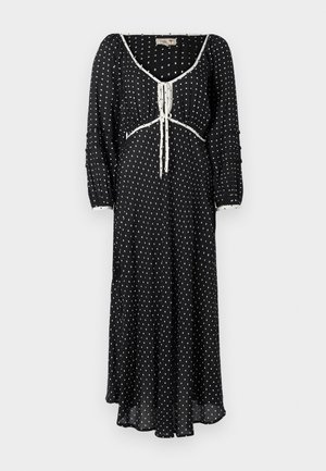 Svart kjole med hvite prikker, lange pufferm, V-hals med snøring og en flytende silhuett. Myk, lett stoff.