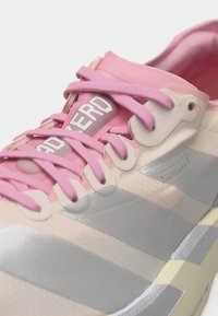 Rosa-beiger Sneaker mit rosa Schnürsenkeln, grauen Streifen an der Seite und dem Schriftzug "ADZERO" auf der Zunge.