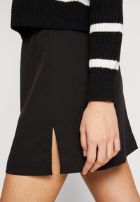 Svart minikjol i slät tyg, med en sidoklyvning, rak fåll och ren söm. Matchas med en svartvit randig tröja.