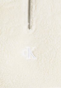 Pullover in finta pelliccia crema con mezza zip argento e logo ricamato "cK" sul petto sinistro. Texture morbida con un aspetto lussuoso e accogliente.