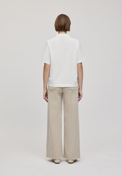 Chemise blanche à manches courtes associée à un pantalon beige à jambes larges. La chemise a un col classique ; le pantalon présente une texture subtile et des poches.