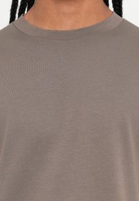Close-up of shoulder and neck wearing a plain taupe crewneck shirt with braided hair visible.