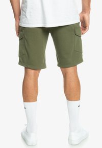 Olivové cargo šortky z bavlny, s bočními kapsami a plochými švy. Nosené s bílými ponožkami a bílými teniskami.
