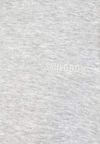 Helles graues Baumwollgewebe mit einer sanften Textur. Verfügt über den dezent gestickten Markennamen "SMILODOX" in einer helleren Nuance.