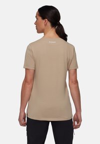 Beige kortærmet skjorte med rund hals. Har et diskret logo på ryggen, glat tekstur og en afslappet pasform.