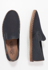 Baskets slip-on en maille navy avec un bout rond, un dessus texturé, des accents en cuir beige, et une semelle en caoutchouc blanche montrant des détails de couture visibles.