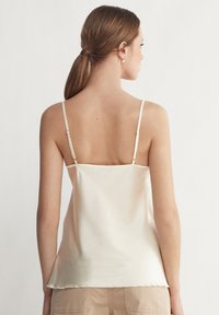 Satin camisole i ljus beige med tunna, justerbara axelband, en rakskuren rygg och en något utfälld nederdel. Slät textur, minimalistisk design.