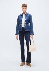 Jachetă din denim cu croială scurtă, nasturi și guler, asortată cu blugi evazați închiși la culoare. Geantă bej, botine maro cu toc.