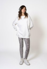 Felpa bianca oversize con un logo rosa discreto, abbinata a leggings grigi con stampa leopardata e sneakers bianche chunky. Completata con le cuffie.