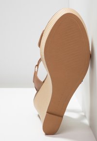 Sandale wedgie marron avec une tige en synthétique, une semelle intérieure texturée beige et une semelle striée. Présente un accent de boucle sur la sangle de la cheville.