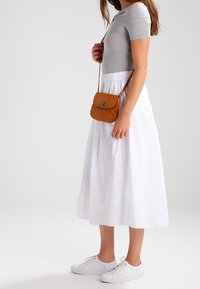 Šedá přiléhavá košile, bílá sukně po kotníky a bílé tenisky. Hnědá kožená crossbody taška s obláčkovým zapínáním. Hladké textury celkově.