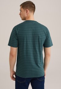 Zöld, rövid ujjú póló geometrikus mintával, kerek nyakkivágással és laza szabással, puha, rugalmas anyagból készült.