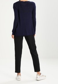 Jersey de canalé azul marino con mangas largas, combinado con pantalones negros ajustados y zapatillas blancas con un divertido estampado de animales.