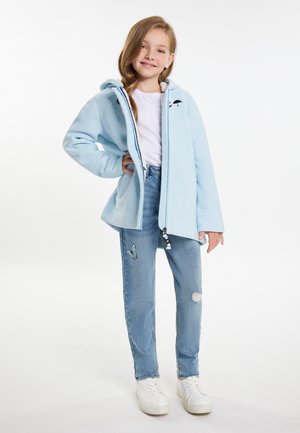 Světle modrá mikina na zip s texturovaným povrchem a kapucí, doplněná o propracované světle modré džíny s výšivkou motýlků a bílé tenisky.