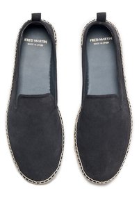 Des chaussures noires en suède à enfiler avec une doublure en cuir lisse, présentant des accents blancs cousus le long de la semelle. Étiquette "Fred Martin" visible à l'intérieur.