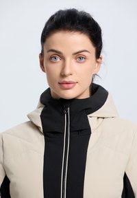 Leichte beigen und schwarze Zip-Jacke mit hohem Kragen, gesteppter Optik und kontrastierenden Einsätzen. Verfügt über einen eleganten, modernen Schnitt.