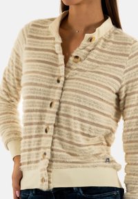 Cardigan de color beige claro con rayas texturizadas, cierre de botones en la parte delantera y un acabado suave. Presenta un dobladillo y puños acanalados para mayor detalle.