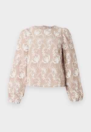 Blouse beige à manches longues avec broderie florale blanche, encolure arrondie, manches bouffantes et poignets élastiques.