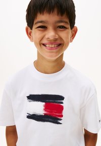 T-shirt en coton blanc avec un motif imprimé de coups de pinceau bleu marine, blanc et rouge. Encolure ronde classique et manches courtes.