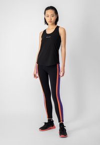 Top atlético negro, ajustado con un cuello redondo. Leggings negros con rayas laterales naranjas y moradas. Zapatillas negras con suelas rosas.