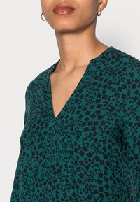 Grön blommönstrad topp med V-ringning och korta ärmar, tillverkad av ett lätt tyg med en mjuk textur.