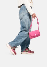 Bolso de cuero rosa con un asa en forma de nudo, de forma rectangular. Llevado con unos vaqueros holgados de color azul claro y zapatillas con un patrón en rosa y marrón.