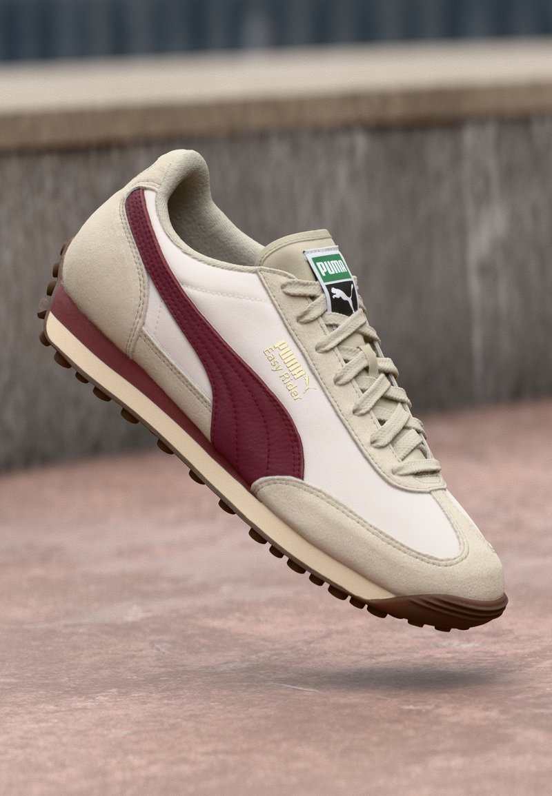 White and maroon athletic shoe with suede and synthetic materials, textured midsole, and rubber outsole featuring circular traction studs.