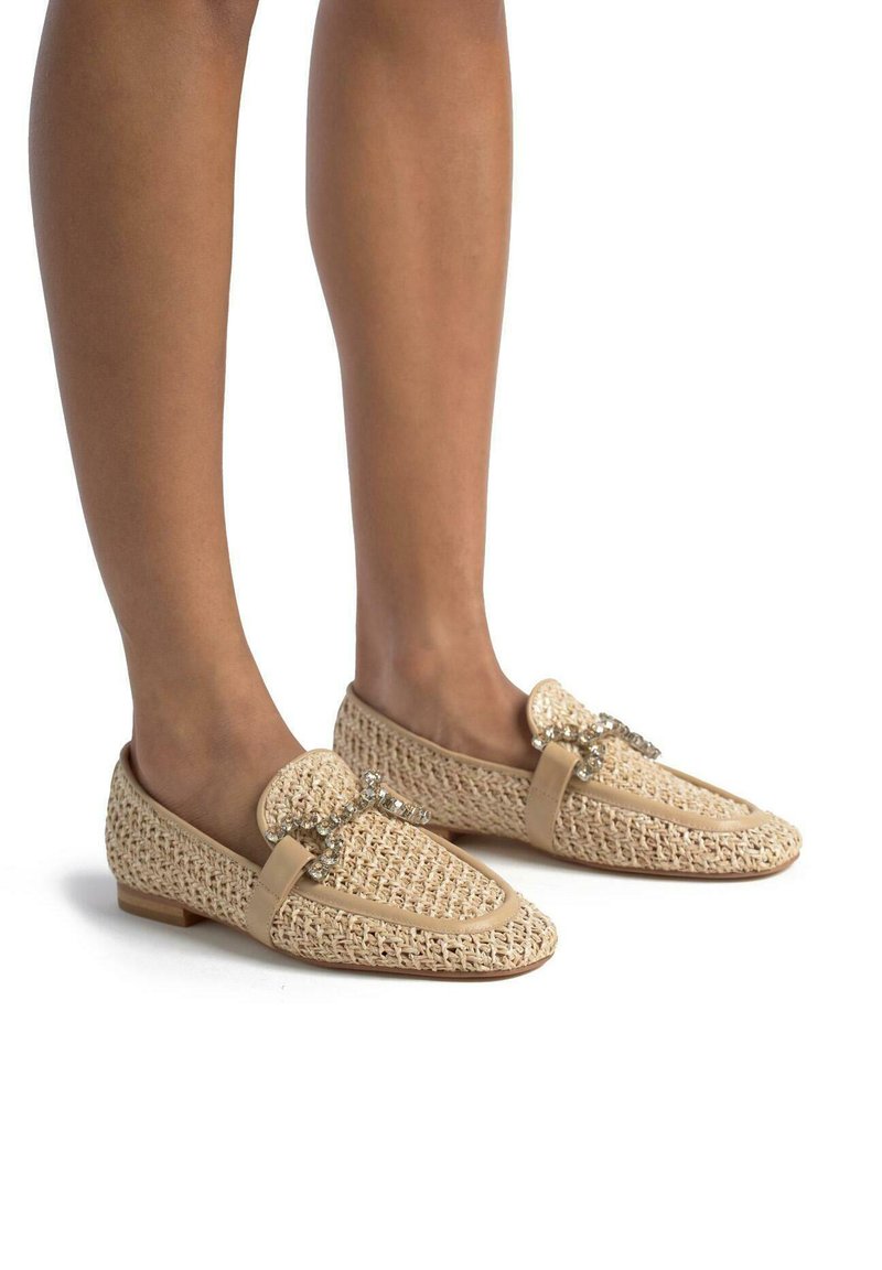 Beige gebreide instappers met een platte hak, voorzien van een decoratieve band en kristalaccenten. Helder textuur en open geweven ontwerp.