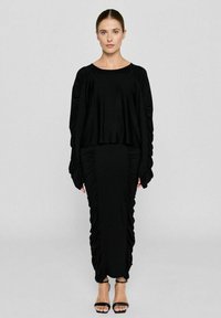 Schwarzes Zweiteiler-Outfit mit einem kurzen Top mit langen, gerafften Ärmeln und einem passenden bodenlangen Rock mit Raffung.
